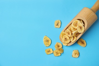 Wooden scoop with banana slices on color background, top view with space for text. Dried fruit as healthy snack