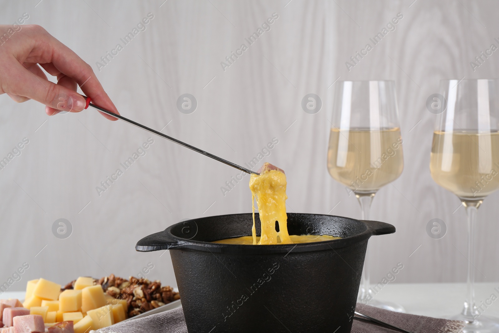 Photo of Dipping piece of ham into fondue pot with tasty melted cheese at table, closeup