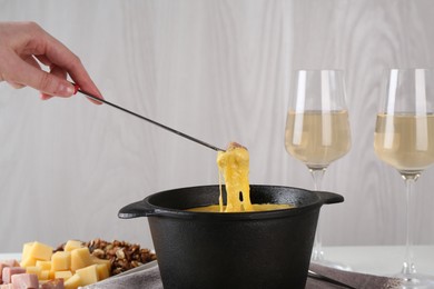 Dipping piece of ham into fondue pot with tasty melted cheese at table, closeup