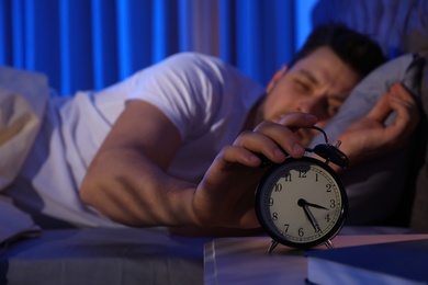 Sleepy man turning off alarm clock in dark room. Bedtime