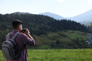 Photo of Tourist with backpack and binoculars enjoying landscape in mountains, back view