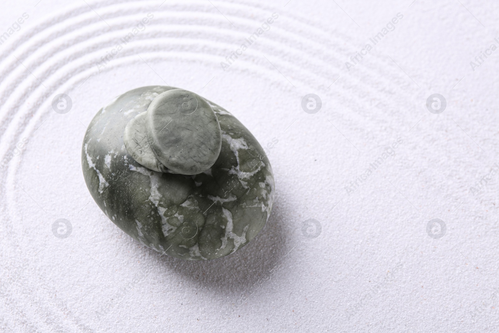 Photo of Zen garden stones on white sand with pattern, top view. Space for text