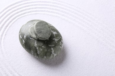 Photo of Zen garden stones on white sand with pattern, top view. Space for text