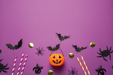 Photo of Flat lay composition with plastic pumpkin basket and paper bats on purple background, space for text. Halloween celebration