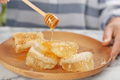 Photo of Woman pouring honey onto honeycombs on plate, closeup