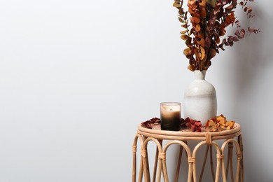 Vase with branches and candle on table near white wall, space for text