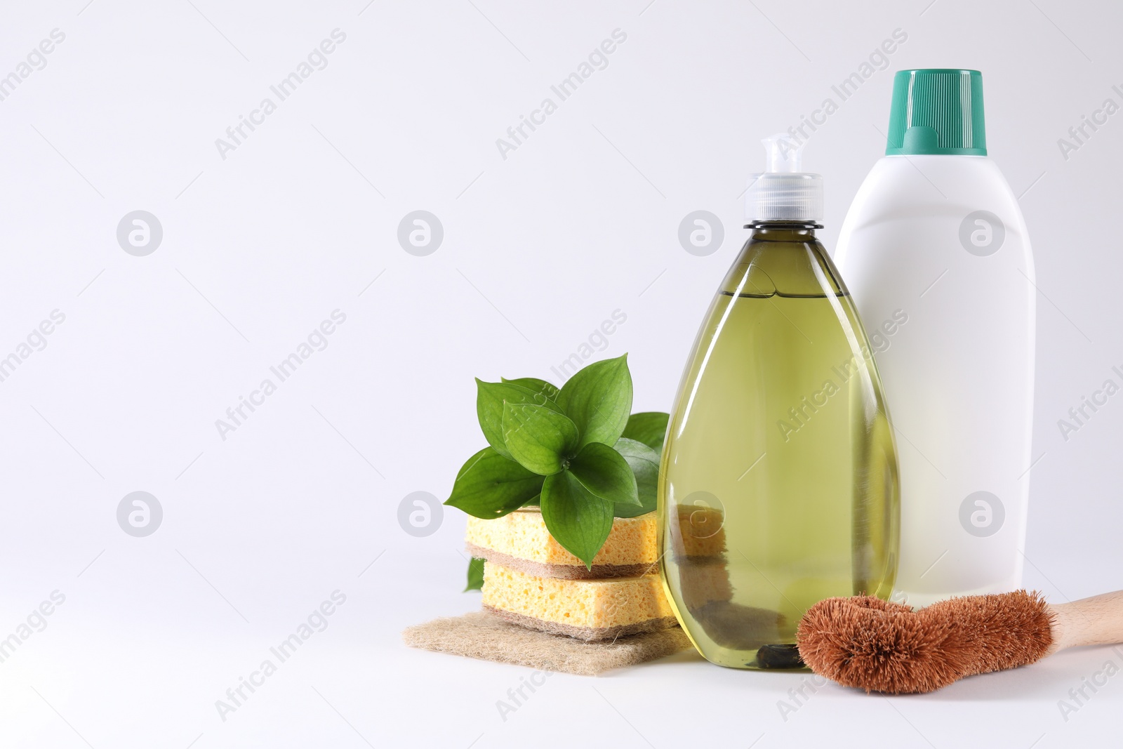 Photo of Bottles of cleaning product, brush, sponges and green leaves on white background