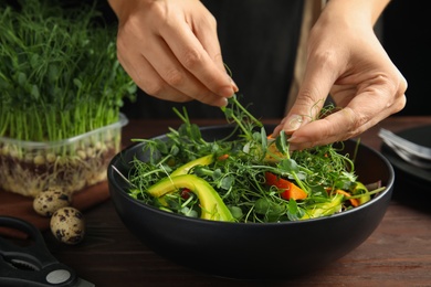 Photo of Woman making salad with fresh organic microgreen at wooden table, closeup