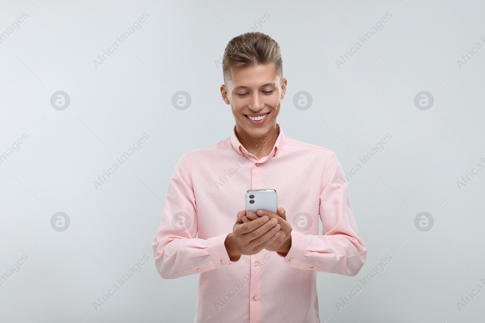 Photo of Happy young man sending message via smartphone on light grey background