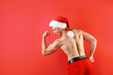 Young muscular man in Santa hat on color background