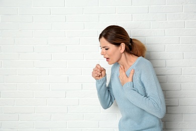 Photo of Woman suffering from cough near brick wall. Space for text