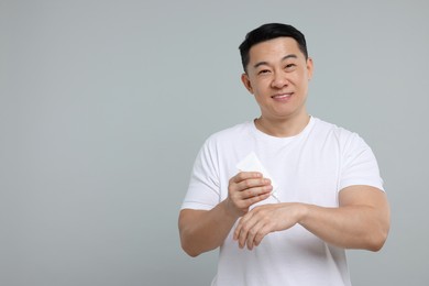 Handsome man applying body cream onto his hand on light grey background. Space for text