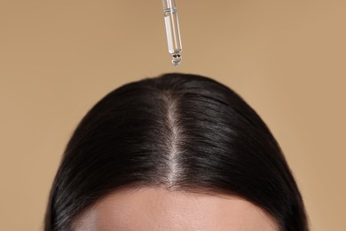 Photo of Woman applying essential oil onto hair roots on beige background, closeup