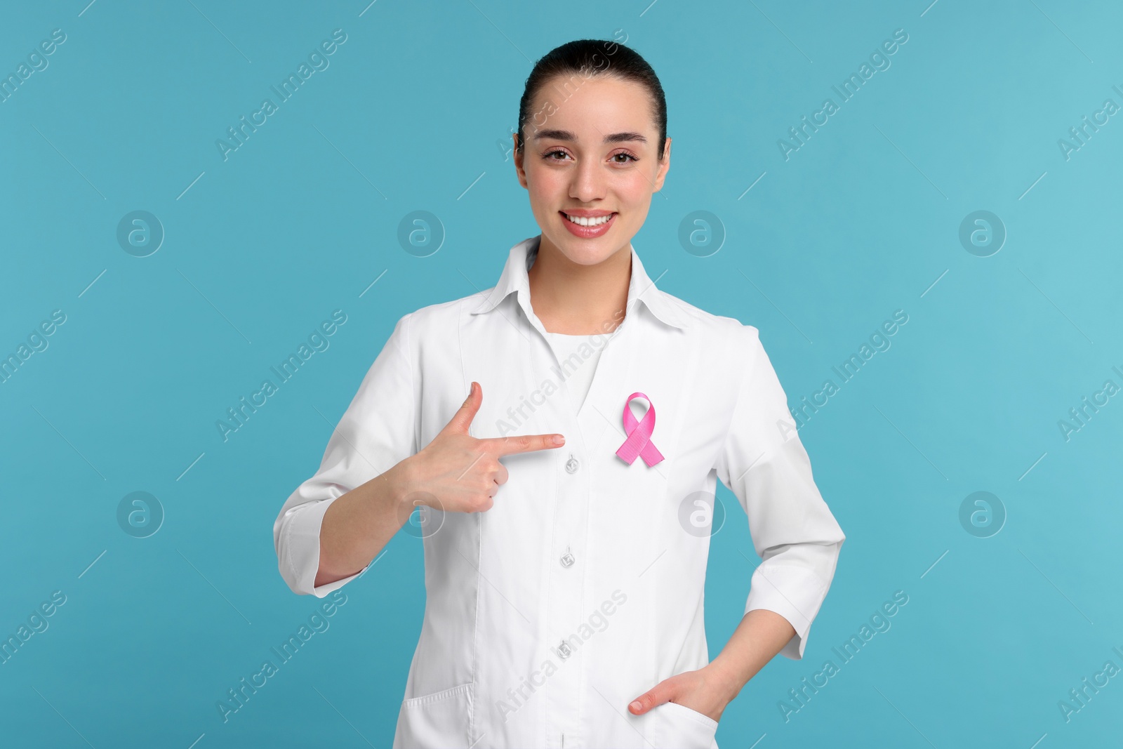 Photo of Mammologist pointing at pink ribbon on light blue background. Breast cancer awareness