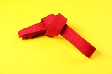Photo of Red karate belt on yellow background, top view