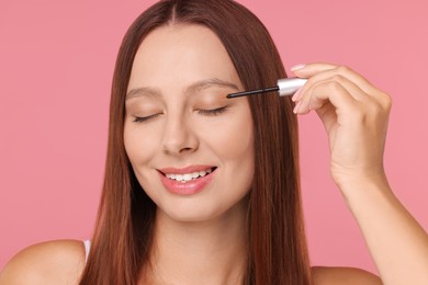 Photo of Beautiful woman applying serum onto eyelashes on pink background
