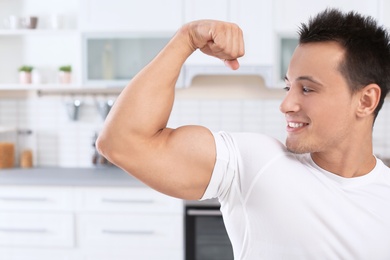 Photo of Athletic man showing bicep in kitchen. Protein shake diet