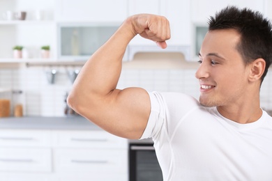 Athletic man showing bicep in kitchen. Protein shake diet