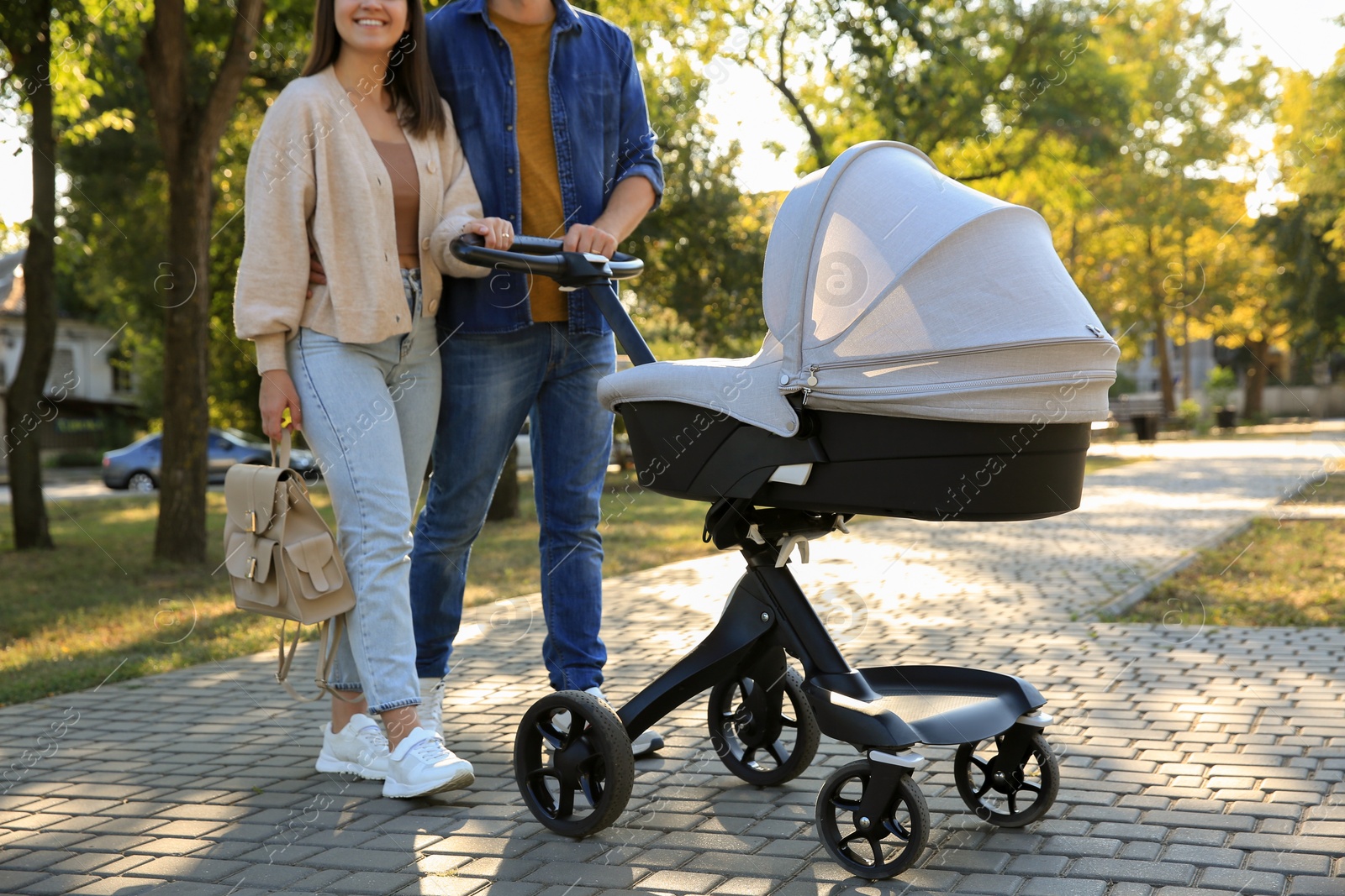 Photo of Parents walking with their baby in stroller at park on sunny day, closeup