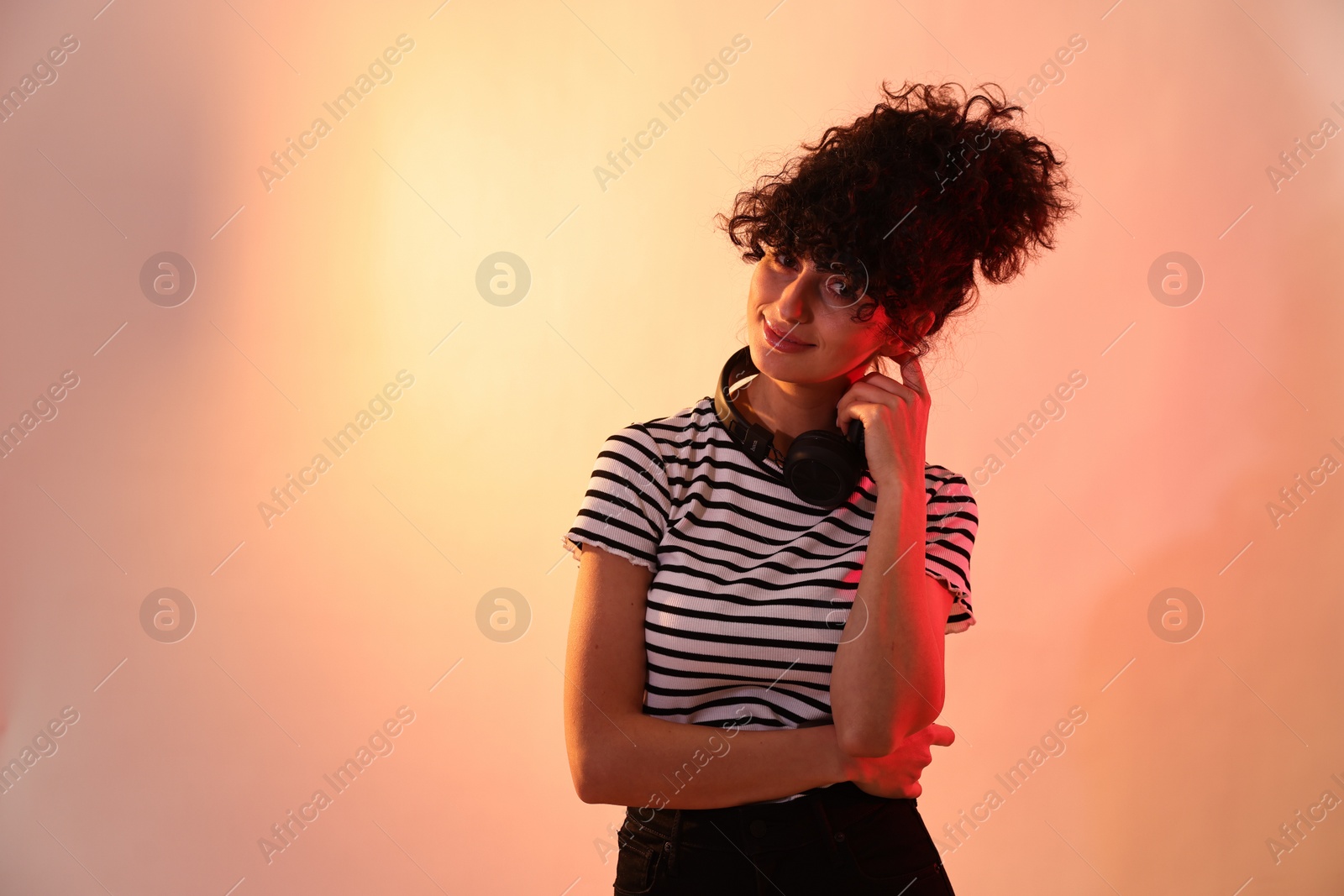 Photo of Beautiful young woman with headphones on color background in neon lights. Space for text