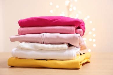 Photo of Stack of folded clothes on wooden table against beige background with blurred lights
