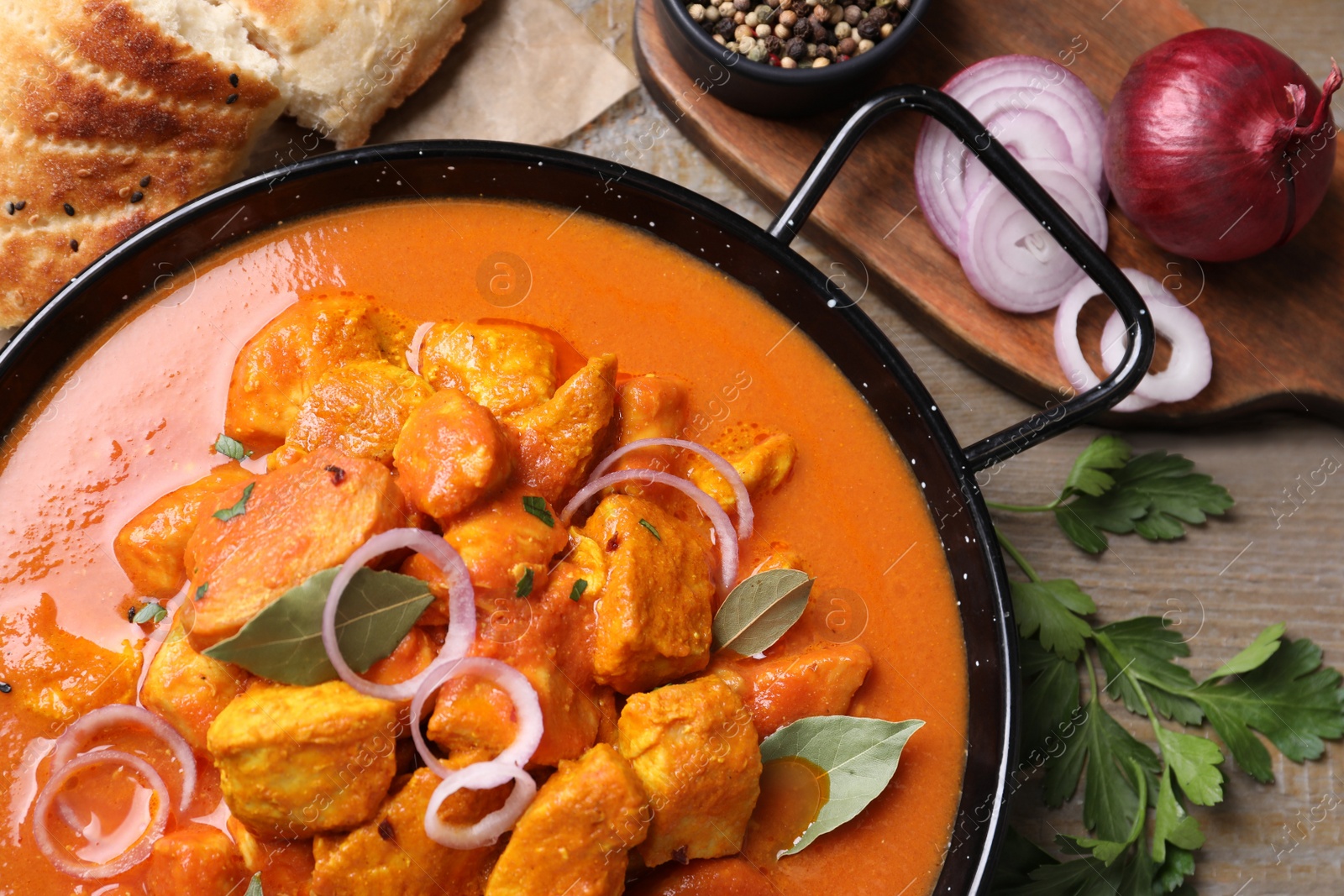 Photo of Delicious chicken curry in pan on wooden table, flat lay