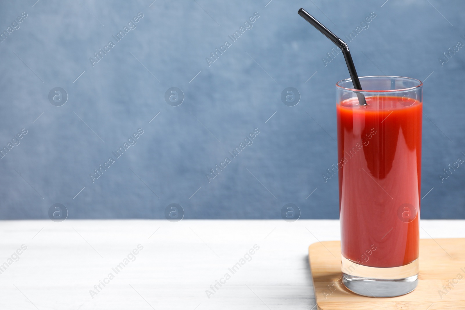 Photo of Delicious fresh tomato juice with straw on white table against light blue background. Space for text