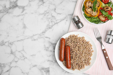 Photo of Tasty buckwheat porridge with sausages on white marble table, flat lay. Space for text
