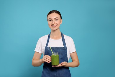 Photo of Beautiful young woman in denim apron with delicious smoothie on light blue background