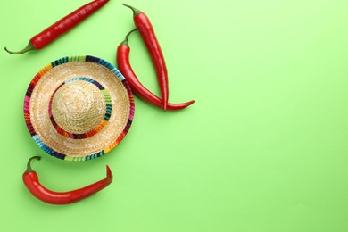 Photo of Mexican sombrero hat and chili peppers on green background, flat lay. Space for text