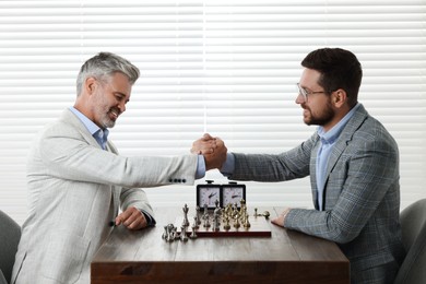 Photo of Men shaking their hands during chess tournament at table indoors