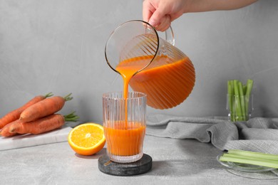 Photo of Woman pouring carrot juice from jug into glass at light grey table, closeup