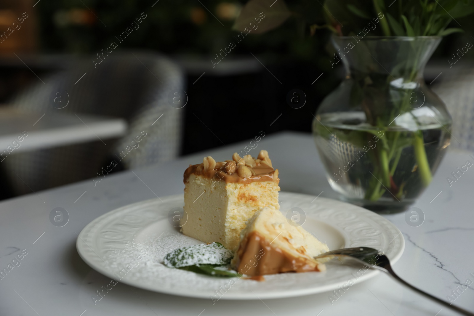 Photo of Tasty dessert and vase with flowers on white table in cafeteria