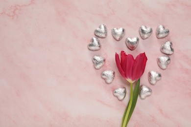 Heart made with delicious chocolate candies and beautiful tulip on pink table, flat lay. Space for text