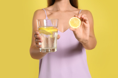 Photo of Young woman with glass of lemon water on yellow background, closeup