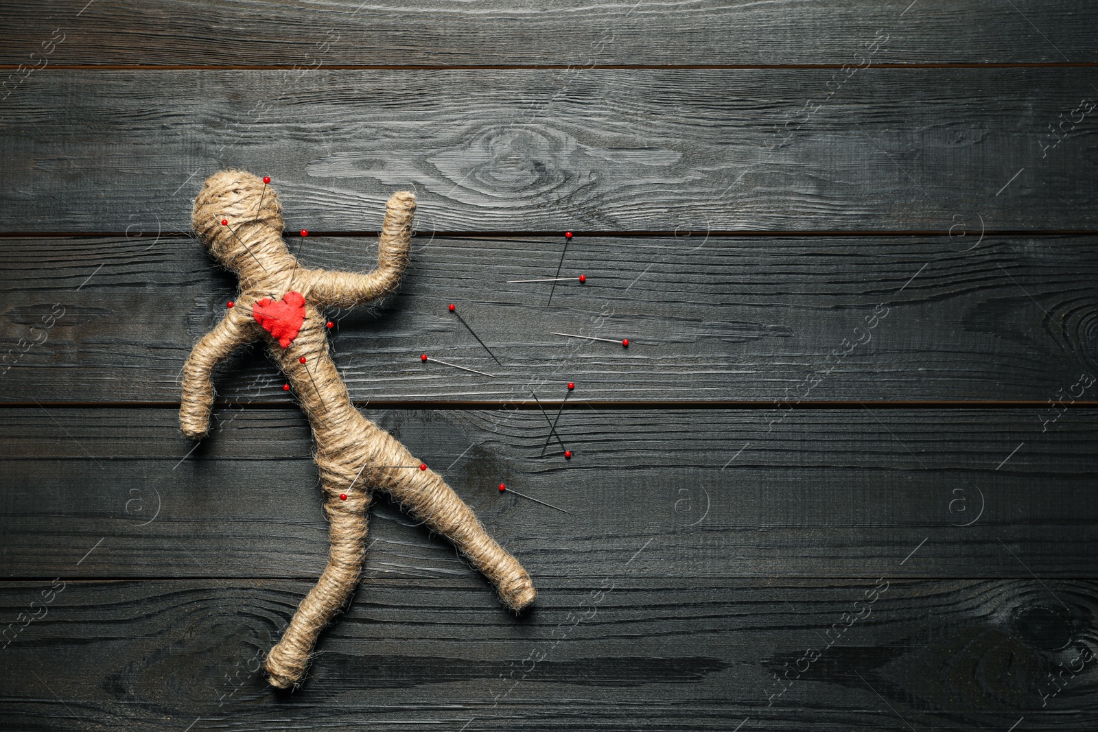 Photo of Voodoo doll and pins on dark wooden table, flat lay. Space for text