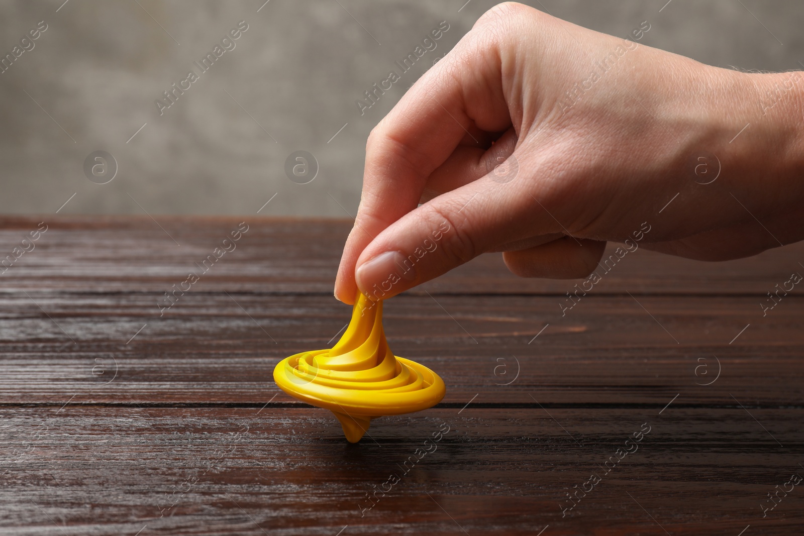 Photo of Woman playing with yellow spinning top at wooden table, closeup