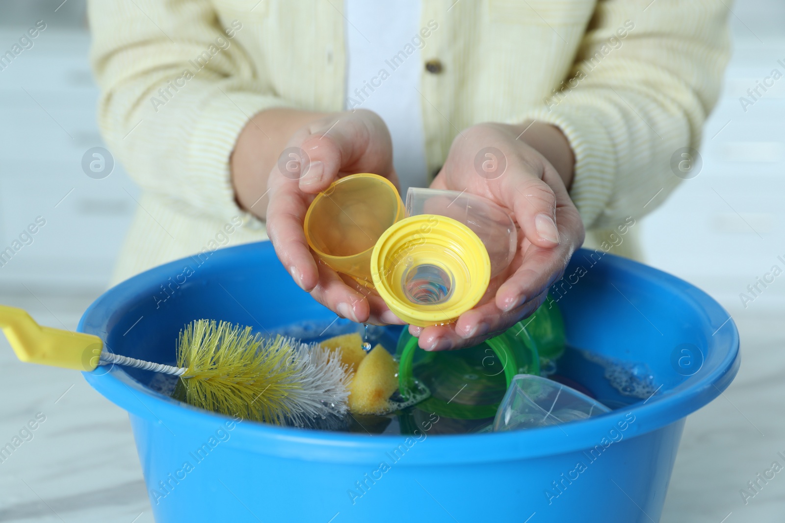 Photo of Woman holding baby bottle nipples above basin with water, closeup. Washing dishes