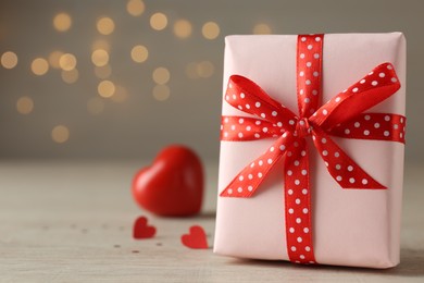 Photo of Beautiful gift box with red hearts on wooden table against blurred lights. Space for text