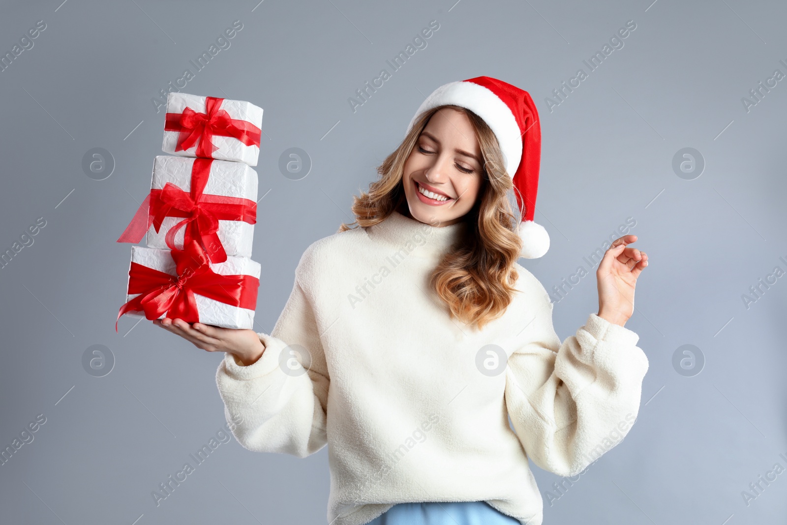 Photo of Beautiful young woman in Santa hat with Christmas presents on light grey background