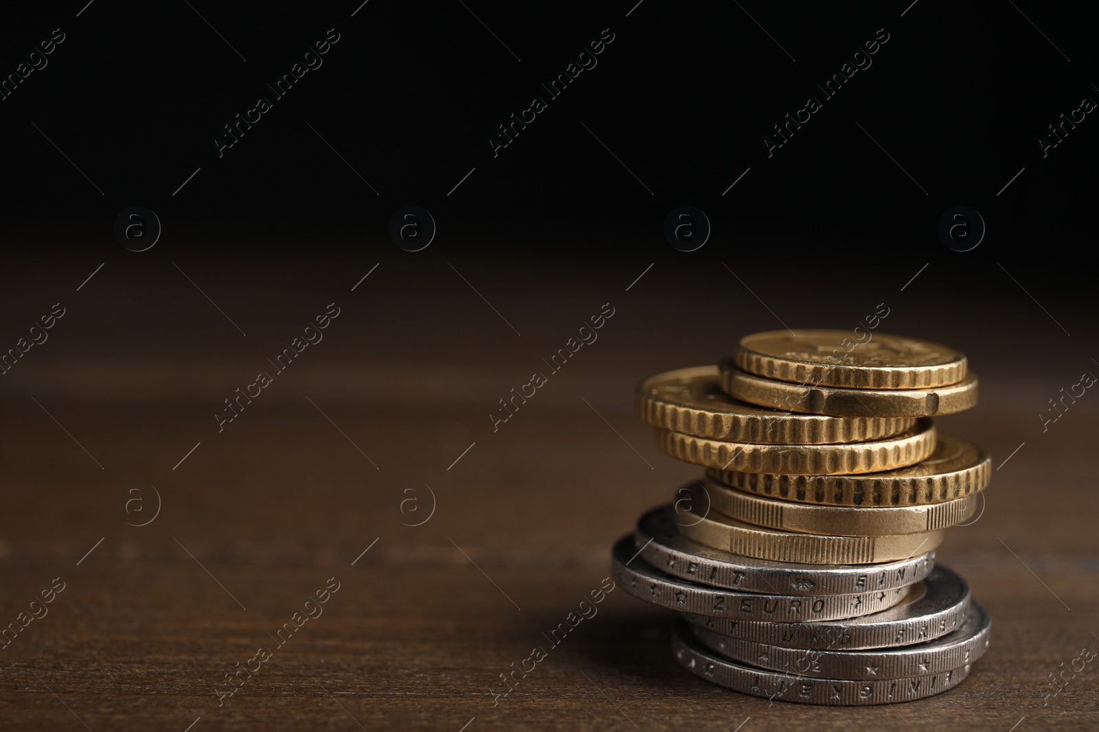 Photo of Many Euro coins stacked on wooden table against black background, space for text