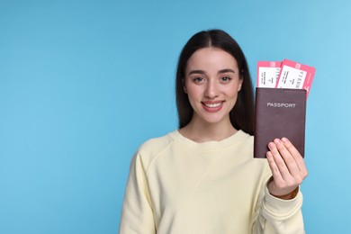 Happy woman showing passport and tickets on light blue background, selective focus. Space for text