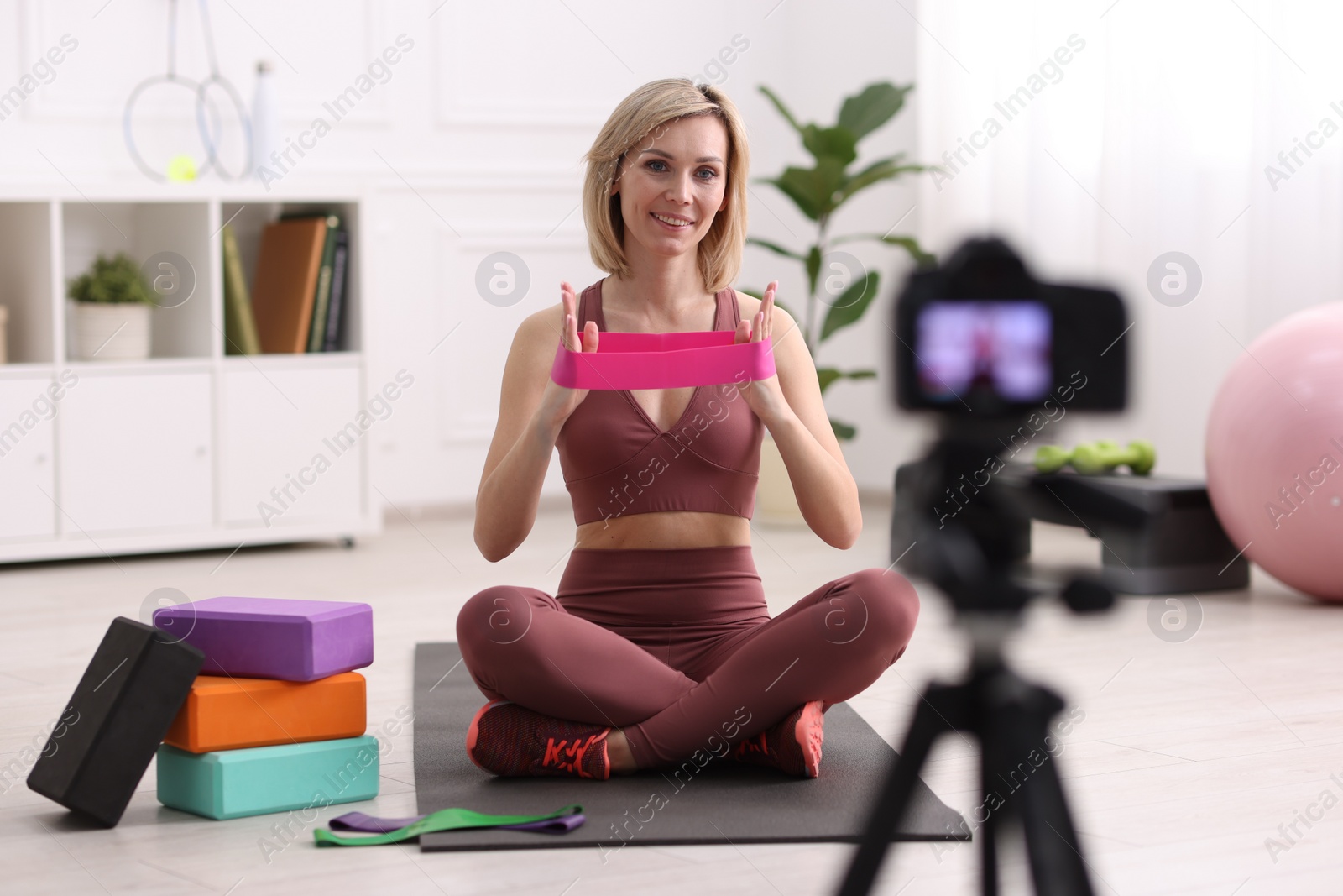 Photo of Smiling sports blogger with with resistance bands recording fitness lesson with camera at home