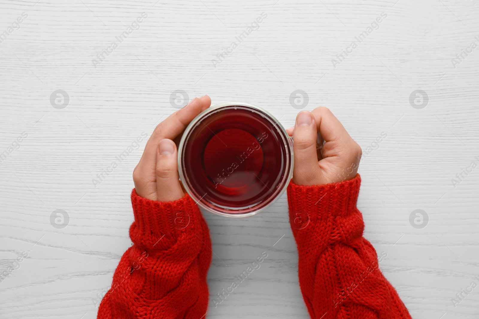 Photo of Woman holding cup of tea at white wooden table, top view. Cozy winter