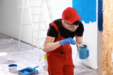 Photo of Male decorator painting wall with brush indoors