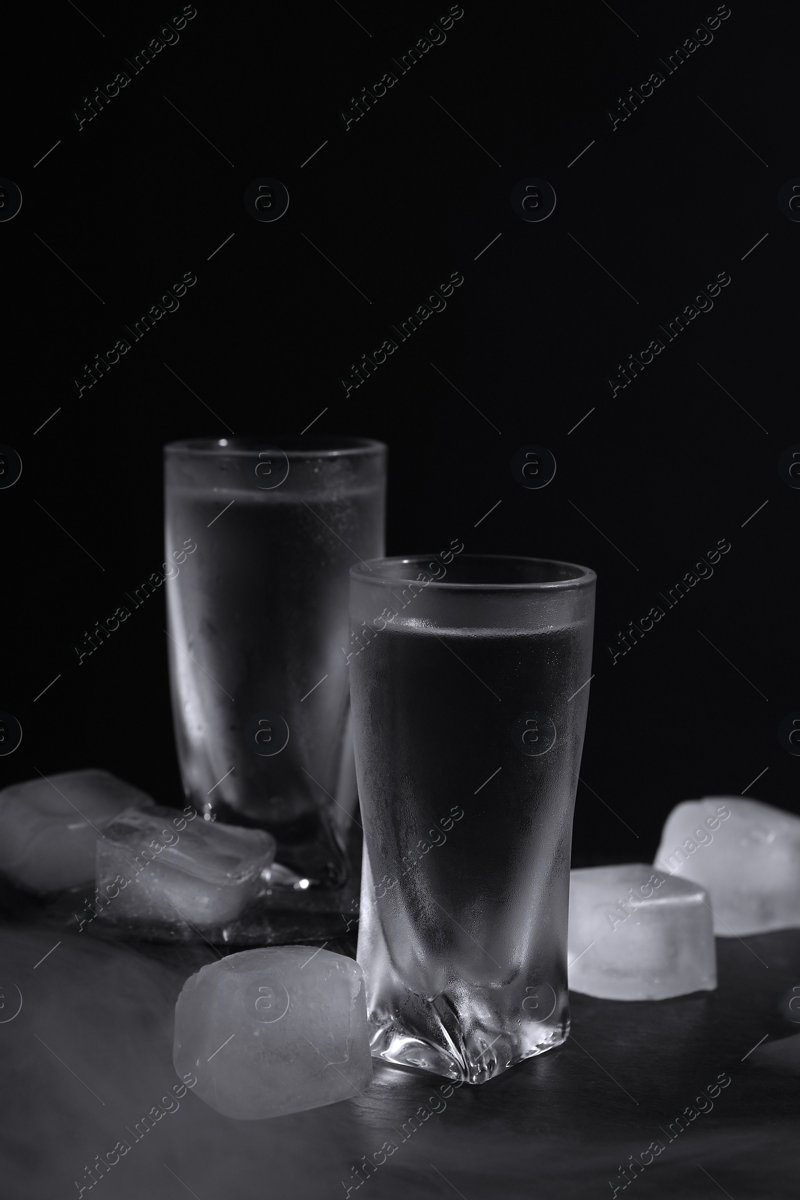 Photo of Vodka in shot glasses with ice on table against black background