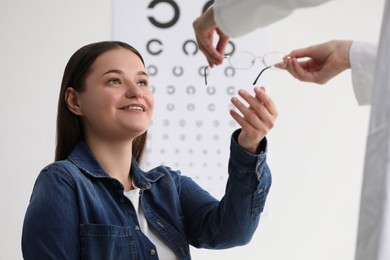 Photo of Vision testing. Ophthalmologist giving glasses to young woman indoors