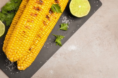 Delicious grilled corn cobs on grey table, flat lay. Space for text