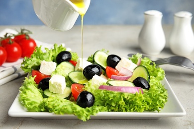 Photo of Dressing tasty fresh Greek salad with olive oil on grey table