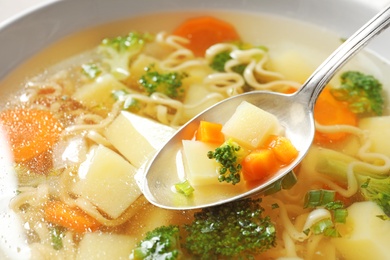 Spoon of fresh homemade vegetable soup over full bowl, closeup